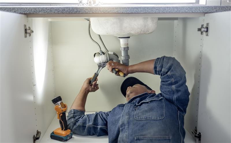 Plumber repairing pipes beneath a bathroom sink in San Mateo